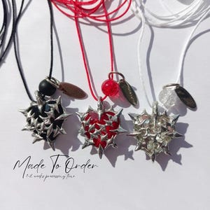 May include: Three necklaces with silver heart pendants featuring a thorny design. The hearts are filled with black, red, and clear resin. The necklaces are on black, red, and white cords. The text "Made To Order" and "1-2 weeks processing time" is below the necklaces.