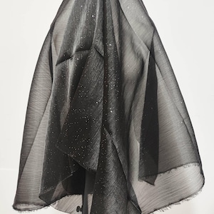 Puede incluir: Tela negra transparente con un brillo sutil. La tela está drapeada sobre un soporte y tiene un borde ligeramente deshilachado.