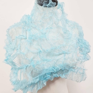 Pode incluir: Um cachecol de tecido azul claro, transparente e com babados. O tecido é em camadas e tem uma textura delicada e arejada.