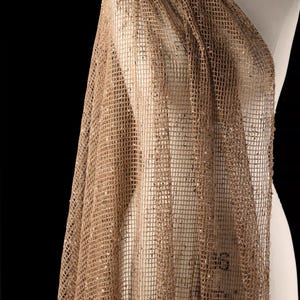 Puede incluir: Una tela drapeada y transparente en un cálido tono marrón dorado. El material tiene un patrón de rejilla, con pequeños adornos dispersos que capturan la luz. La tela se muestra sobre un maniquí, mostrando su caída y textura.