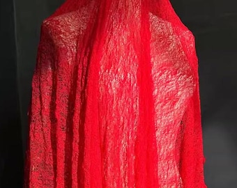 May include: A draped, bright red fabric with a textured, semi-sheer appearance. The fabric is arranged to resemble a hooded garment or veil, with visible folds and a flowing design. The overall effect suggests a costume or decorative textile.