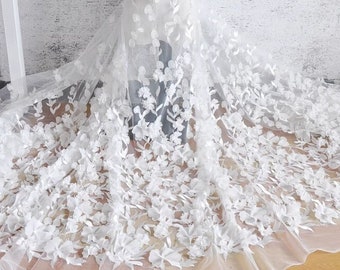 May include: White floral lace fabric with 3D flowers. The lace is delicate and intricate, with a soft, flowing texture. The flowers are raised and have a realistic appearance.