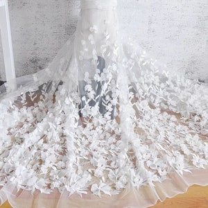 Puede incluir: Tela de encaje floral blanca con flores 3D. El encaje es delicado e intrincado, con una textura suave y fluida. Las flores son en relieve y tienen un aspecto realista.