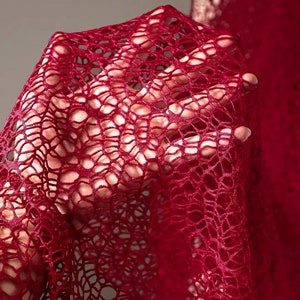 May include: A close-up of a red crocheted fabric with a delicate, intricate pattern. The fabric is soft and flowing, with a subtle sheen.