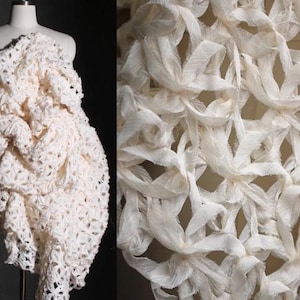 Puede incluir: Un vestido blanco de crochet con un diseño único y texturizado. La tela está hecha de tiras finas y delicadas de material que se tejen juntas para crear un efecto tridimensional.
