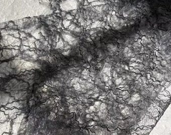 May include: Close-up of a piece of dark gray, sheer fabric with a complex, web-like pattern. The fabric appears delicate and textured, with a slightly wrinkled appearance. The material is likely used for decorative purposes.