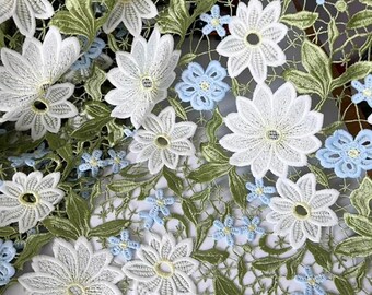 Puede incluir: Tela de encaje floral blanca y azul con un patrón delicado. La tela presenta un diseño repetitivo de grandes flores blancas con flores azules más pequeñas intercaladas.