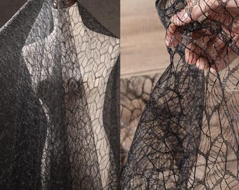 May include: Black spiderweb mesh fabric with a delicate, intricate pattern. The fabric is sheer and has a slightly glittery finish.