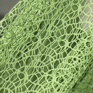 Puede incluir: Primer plano de una tela verde claro de tejido abierto. La tela tiene una apariencia de red con un patrón repetitivo de formas redondeadas interconectadas. El color es un verde vibrante y primaveral.
