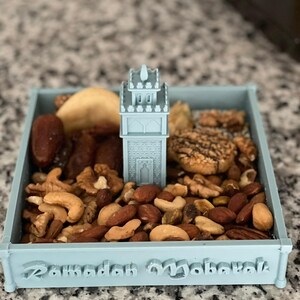 May include: A light blue tray with a 3D printed mosque design in the center. The tray is filled with a variety of nuts and dried fruit. The tray has the words "Ramadan Mubarak" inscribed on the bottom.