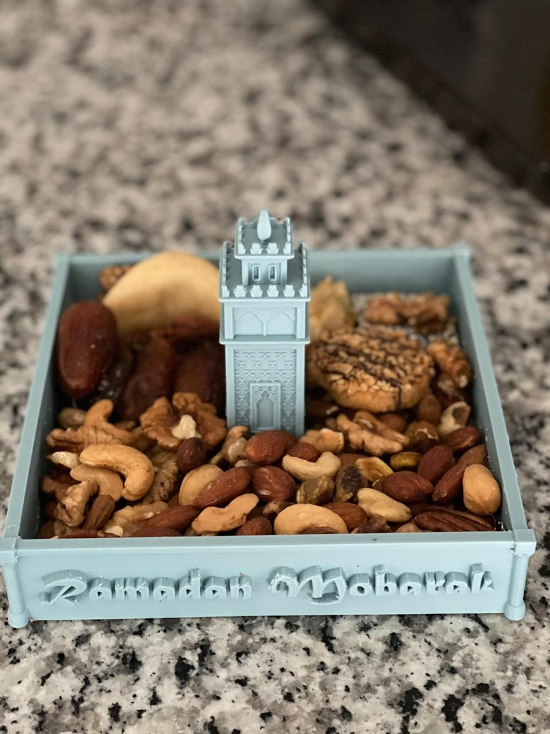 May include: A light blue tray with a 3D printed mosque design in the center. The tray is filled with a variety of nuts and dried fruit. The tray has the words "Ramadan Mubarak" inscribed on the bottom.