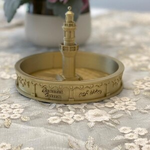 May include: A gold-colored decorative dish with a miniature mosque in the center. The dish has the words "Ramadan Kareem" and "رمضان كريم" inscribed on it.