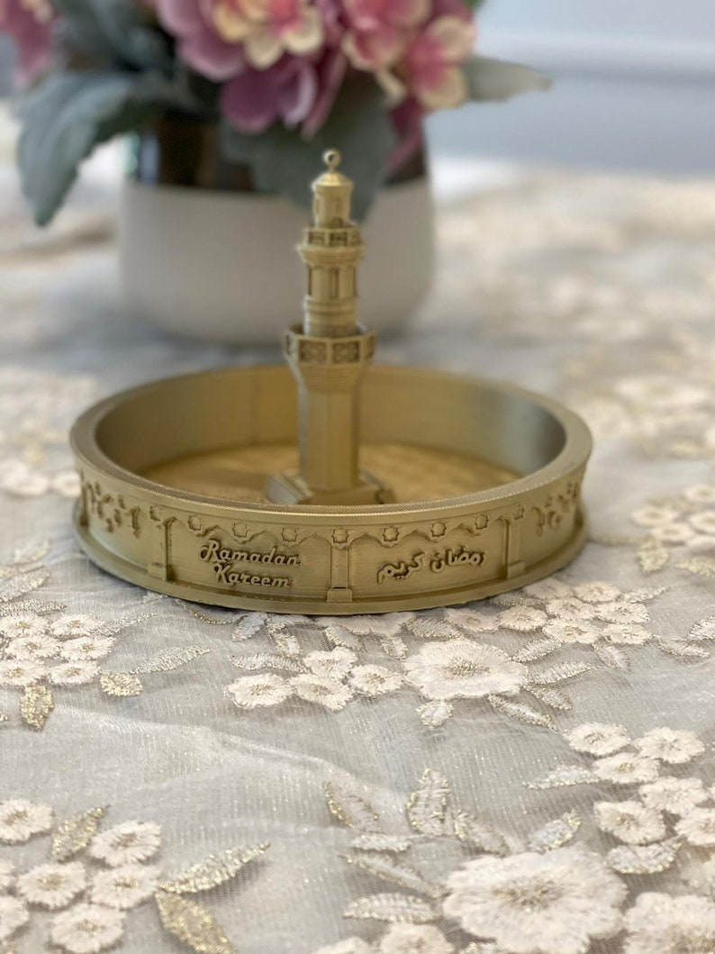 May include: A gold-colored decorative dish with a miniature mosque in the center. The dish has the words "Ramadan Kareem" and "رمضان كريم" inscribed on it.