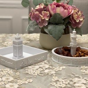 May include: Two white ceramic dishes with a mosque design. One dish has dates and almonds inside. The other dish has a small mosque figurine inside. Both dishes have the text "Ramadan Kareem" in Arabic and English.