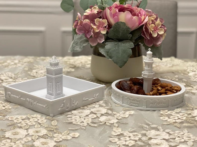 May include: Two white ceramic dishes with a mosque design. One dish has dates and almonds inside. The other dish has a small mosque figurine inside. Both dishes have the text "Ramadan Kareem" in Arabic and English.