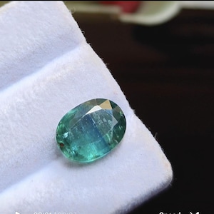 Peut inclure: Une pierre précieuse de taille ovale avec une surface à facettes présentant un dégradé de teintes bleu sarcelle profond et vert forêt. La pierre présente des caractéristiques de clarté interne et des reflets lumineux sur sa surface polie.