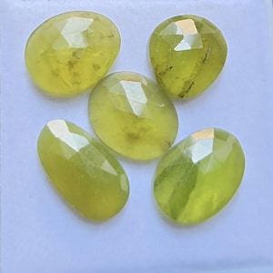 Peut inclure: Cinq pierres précieuses ovales à facettes d'une couleur vert citron éclatante. Chaque pierre présente une surface polie à facettes multiples qui reflète la lumière, révélant des inclusions naturelles et des nuances de vert jaune translucide.