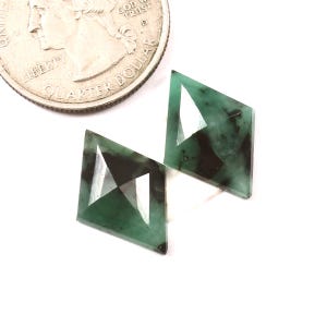 May include: Two emerald green faceted gemstones in a kite shape.