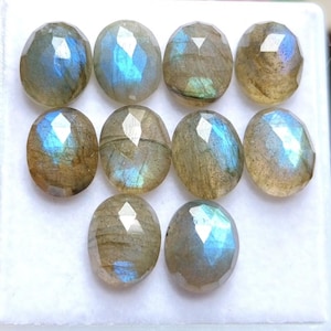 Peut inclure: Dix pierres précieuses de labradorite de forme ovale disposées sur trois rangées. Chaque pierre présente une surface à facettes avec une couleur de base brun grisâtre et des reflets bleus irisés qui changent selon la lumière.