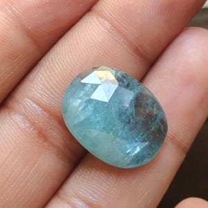 Pode incluir: Uma gema de água-marinha azul claro com corte facetado. A gema tem formato oval e tem uma aparência translúcida.