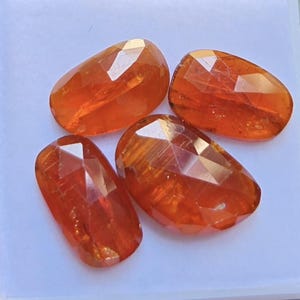 Peut inclure: Quatre pierres précieuses orange de forme ovale et à facettes avec une finition polie. Chaque pierre présente une teinte ambrée translucide et vibrante avec des motifs de coupe géométriques qui reflètent la lumière, disposées en groupe.