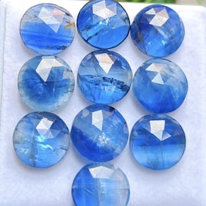 May include: Ten round, faceted blue kyanite gemstones arranged in a grid pattern. Each stone features a polished, circular top with a geometric rose-cut surface, displaying varying shades of deep to light blue with natural internal inclusions.