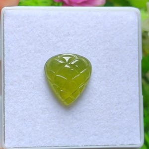 May include: A faceted, pear-shaped gemstone in a vibrant, translucent green hue. The gem is set against a white background, showcasing its intricate cut and clarity. The gemstone's surface reflects light, highlighting its geometric pattern.