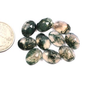 Puede incluir: Una colección de diez piedras preciosas de ágata musgosa facetadas. Las piedras de forma ovalada son una mezcla de verde y blanco con una apariencia translúcida.