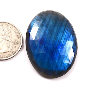 May include: A large, oval-shaped, blue labradorite gemstone with a faceted cut. The gemstone has a dark blue color with iridescent flashes of green and gold.