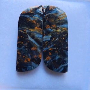 May include: Two polished, semi-circular stones with a striking pattern. The stones feature a dark blue base with swirling veins of gold and lighter blue, creating a marbled effect. The stones are likely used for jewelry or decorative purposes.