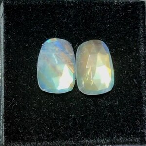 May include: Two iridescent, oval-shaped gemstones with a faceted cut. The gems display a range of colors, including blue, yellow, and green, and are set against a black background. These gemstones are suitable for jewelry making.