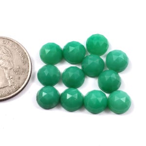 May include: A group of 12 green gemstone cabochons, each with a faceted, rounded shape. The cabochons are arranged in a loose cluster, with some overlapping.