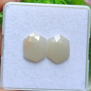 Può includere: Due pietre preziose esagonali giallo pallido con superfici sfaccettate sono esposte in una scatola bianca. Le gemme hanno una qualità sottile e traslucida e sono poste su uno sfondo bianco. Le gemme sono probabilmente per la creazione di gioielli.