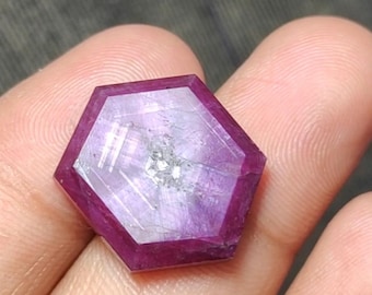Puede incluir: Una gema hexagonal facetada, de un tono magenta intenso. La gema tiene una superficie pulida con inclusiones internas y un centro más claro, casi translúcido. Los bordes están bien definidos y la forma es simétrica.