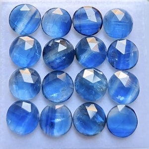 May include: Sixteen round, faceted blue gemstones arranged in a four-by-four grid. Each stone features a polished, circular top with a geometric, multi-faceted cut that reflects light, displaying varying shades of translucent and deep royal blue.