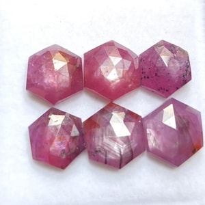 May include: Six loose, hexagonal-cut pink gemstones arranged in two rows of three. Each stone features a faceted surface with varying degrees of translucency, internal inclusions, and color saturation ranging from light to deep magenta pink.
