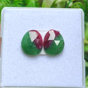 Könnte beinhalten: Zwei ovale Edelsteine mit einer Mischung aus grünen und roten Farben. Die Steine sind facettiert und vor einem weißen Hintergrund platziert.