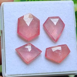 Op de afbeelding: Vier roze edelstenen met facetten in diverse vormen, waaronder een zeshoek, twee ruitvormen en een vijfhoek. De edelstenen worden getoond in een witte plastic houder, wat hun helderheid en kleur benadrukt. Geschikt voor sieraden.
