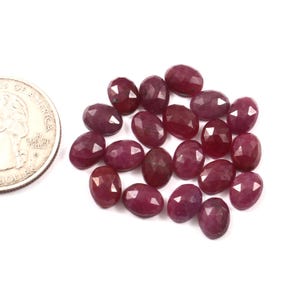 Puede incluir: Un montón de 18 piedras preciosas de rubí facetadas de color rojo intenso. Las piedras son de forma ovalada y tienen un acabado liso y pulido.