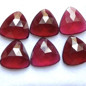 Peut inclure: Six pierres précieuses facettées en vrac d'une couleur rouge profond et vibrante. Chaque pierre présente une forme triangulaire aux coins arrondis et une surface polie à facettes multiples qui reflète la lumière, créant un éclat brillant.