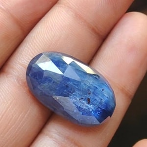 May include: A deep blue oval-shaped gemstone with a faceted cut. The gemstone has a striated pattern and is set in a silver ring.