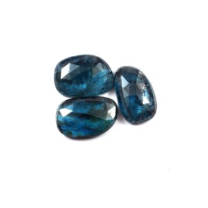 Op de afbeelding: Drie gefacetteerde blauwe kyaniet edelstenen met een ovale vorm. Elke steen vertoont een diepe, doorschijnende blauwe kleur met zichtbare donkere insluitingen en een gepolijst oppervlak dat licht reflecteert over de vele platte, geometrische facetten.