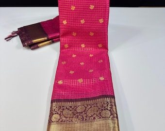 May include: A vibrant pink saree with a gold floral border and gold leaf-like patterns. The saree has a grid-like pattern throughout the pink fabric. The border is a deep burgundy with gold floral designs and a gold band.