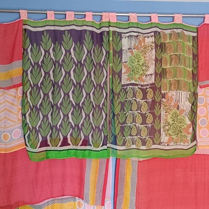 May include: A set of colourful curtains made from repurposed fabric. The curtains are hung on a silver rod and feature a variety of patterns, including floral, paisley, and geometric designs. The curtains are a mix of pink, red, green, yellow, and blue.