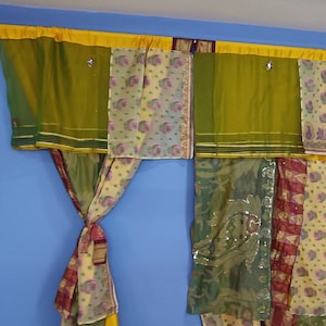 May include: A set of colourful curtains made from different fabrics, including green, yellow, and brown. The curtains are hung on a rod and are tied back on each side.
