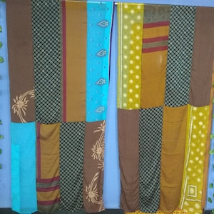 May include: Two long panels of fabric made from different patterned pieces of fabric sewn together. The panels are brown, blue, green, and yellow. The panels are hanging on a blue wall.