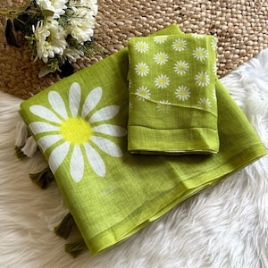May include: A green textile set featuring a large daisy print and a smaller daisy pattern. The set includes a folded piece and a larger unfolded piece with tassels. The background is a woven mat and white faux fur.