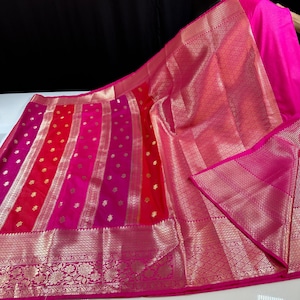 May include: A vibrant pink and red textile with gold accents. The fabric features vertical stripes of varying shades of pink and red, with gold floral patterns and borders. The design includes a detailed, ornate gold border.