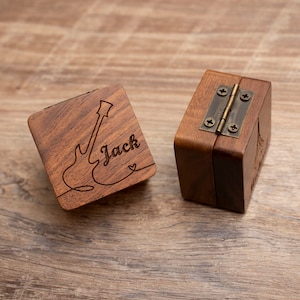 K&ouml;nnte beinhalten: Zwei Holzk&auml;stchen f&uuml;r Ringe mit einem Gitarrenmotiv und dem eingravierten Namen "Jack" auf einem K&auml;stchen. Die K&auml;stchen haben ein Messing Scharnier.