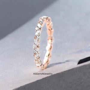 Op de afbeelding: Roségouden ring met een doorlopende band van afwisselende ronde en marquise-geslepen heldere edelstenen. De ring staat tegen een zachte grijze achtergrond. De tekst "ASGemsNJewelry" is onderaan zichtbaar.